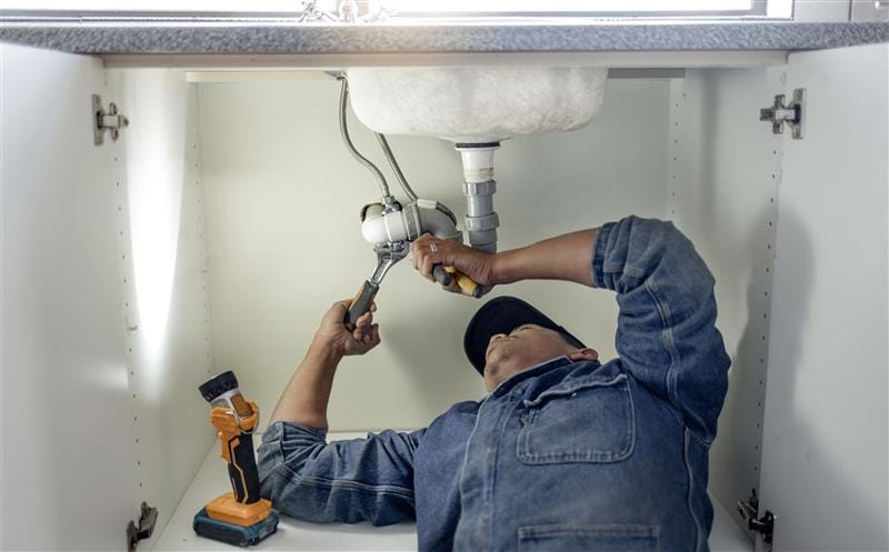 Plumber repairing pipes beneath a bathroom sink in Beaumont