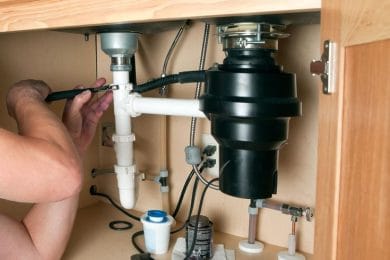 Plumber repairing a garbage disposal beneath a kitchen sink in Beaumont