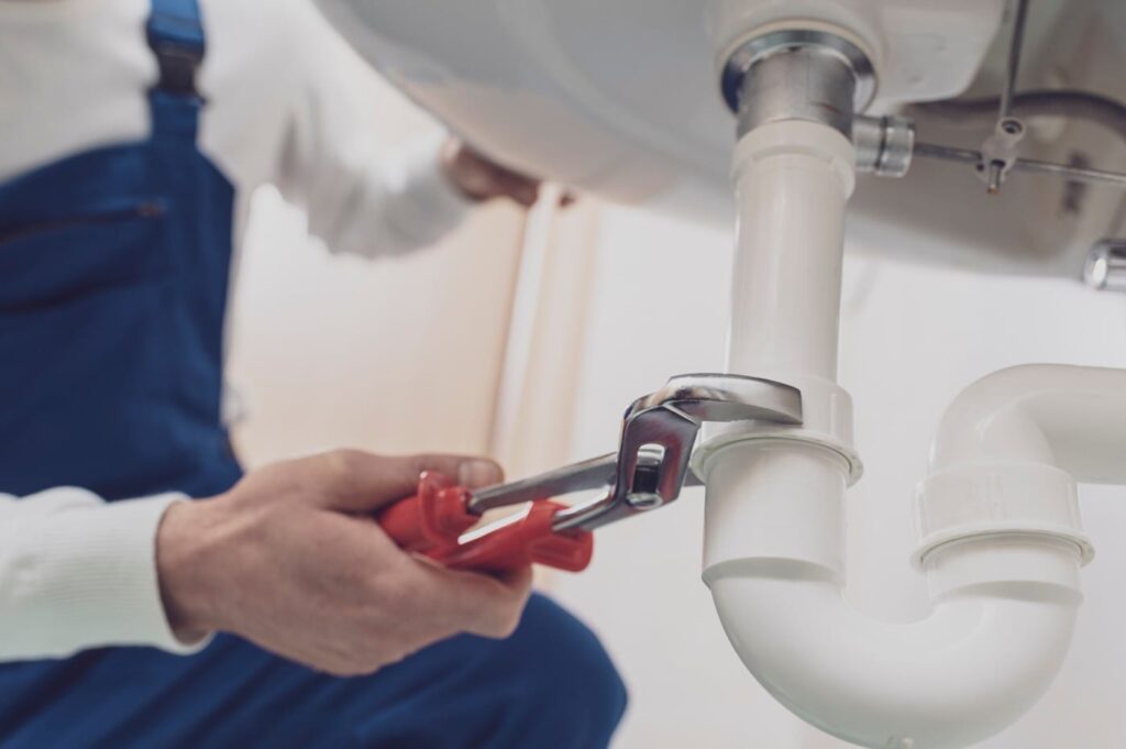 Plumber repairing a white drain pipe beneath a sink in Beaumont