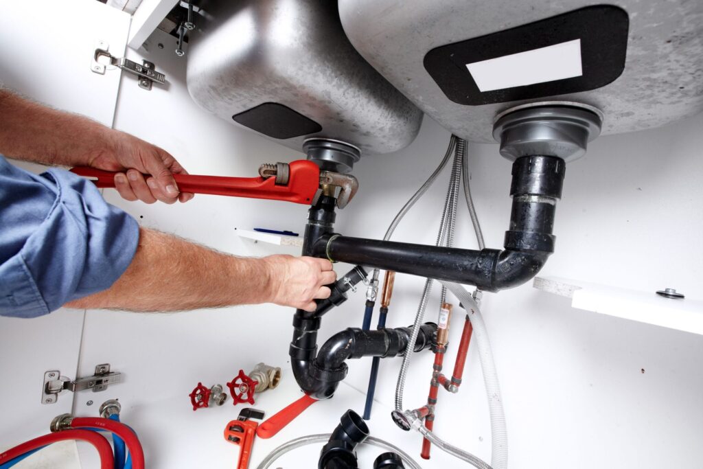 Plumber repairing drain pipes beneath a kitchen sink in Beaumont